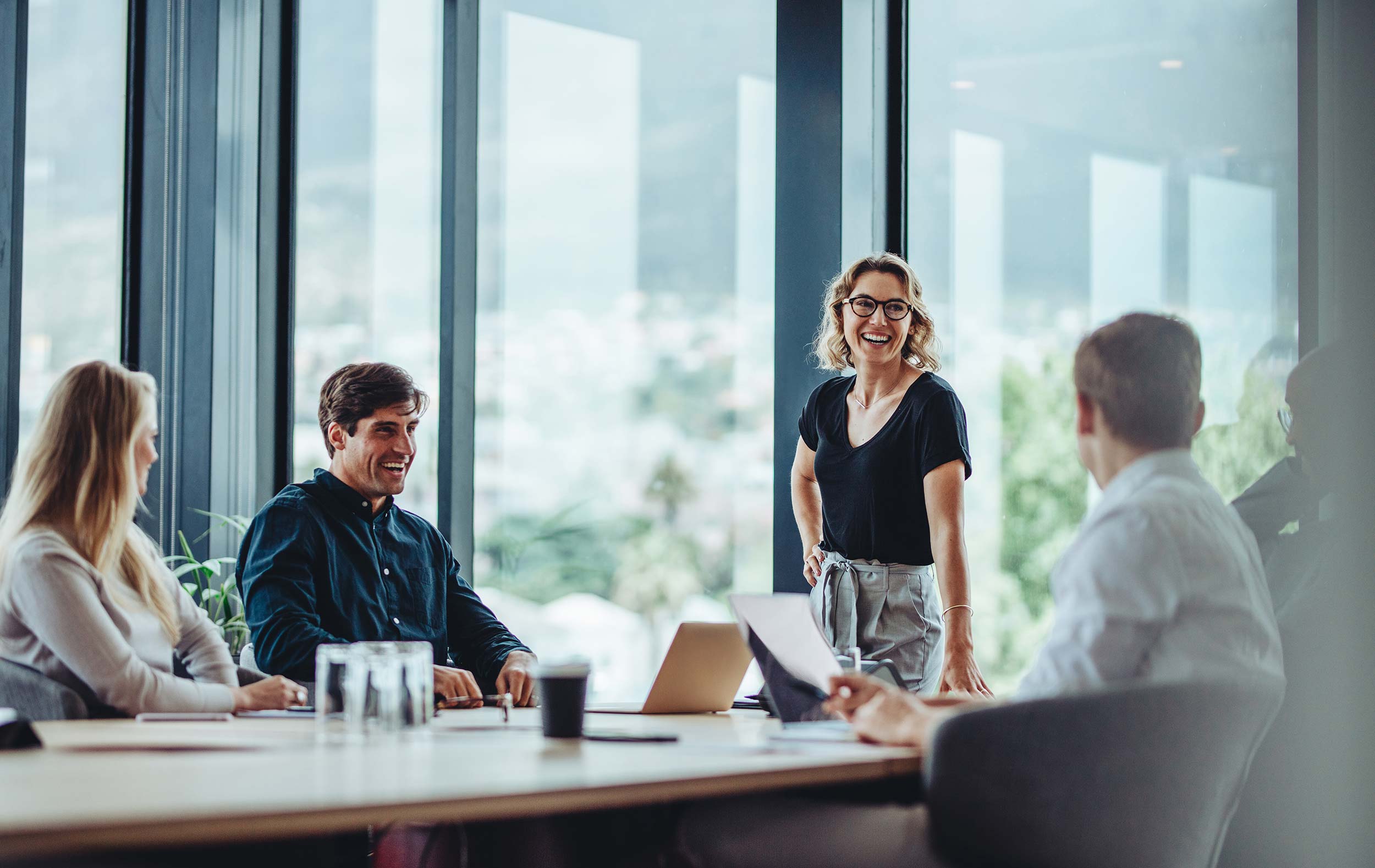 A group of business people sit around a conference table with one standing to lead a funny topic