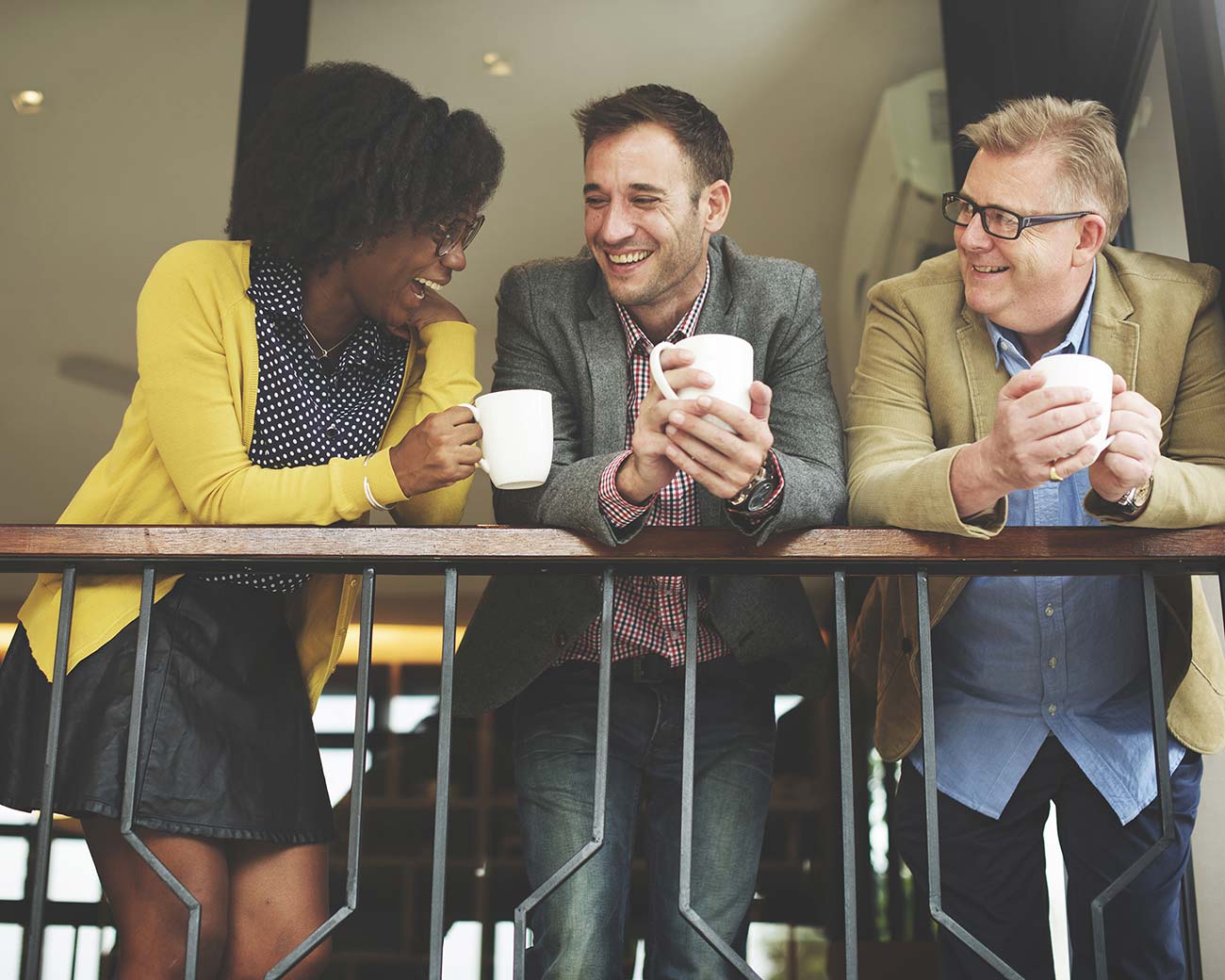 Three business professionals on a break discussing a previous session. They are laughing and holding coffee