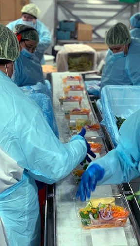 Photo of workers wearing blue smocks inside Fresh Texas's San Antonio produce facility packing fresh produce