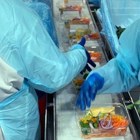 Photo of workers wearing blue smocks inside Fresh Texas's San Antonio produce facility packing fresh produce