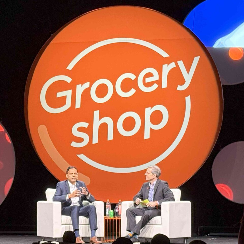 Covers Two men speak in large chairs in front of a background from Grocery Shop