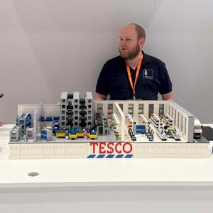 Tesco employee stands behind a lego model of a fully automated supply system