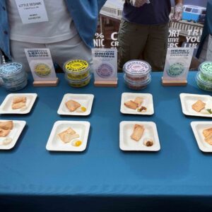 Multiple colors of dips sit in round containers on a blue table with sample trays