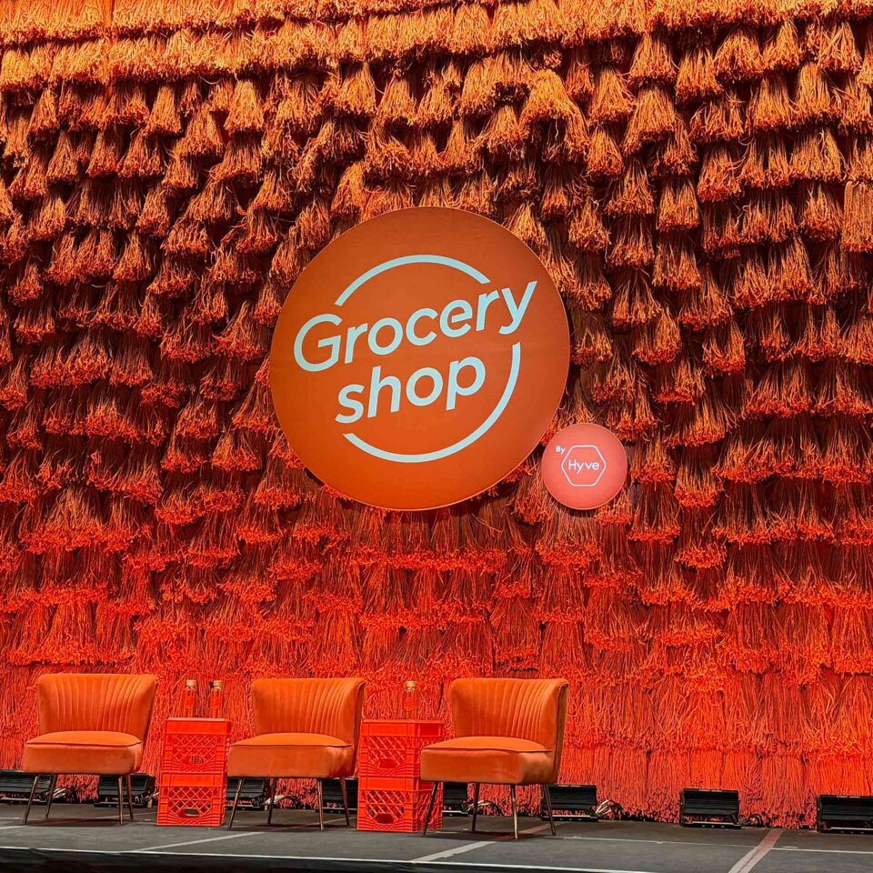 Cover Orange mop heads hung as a backdrop behind orange grocery shop logo and orange chairs