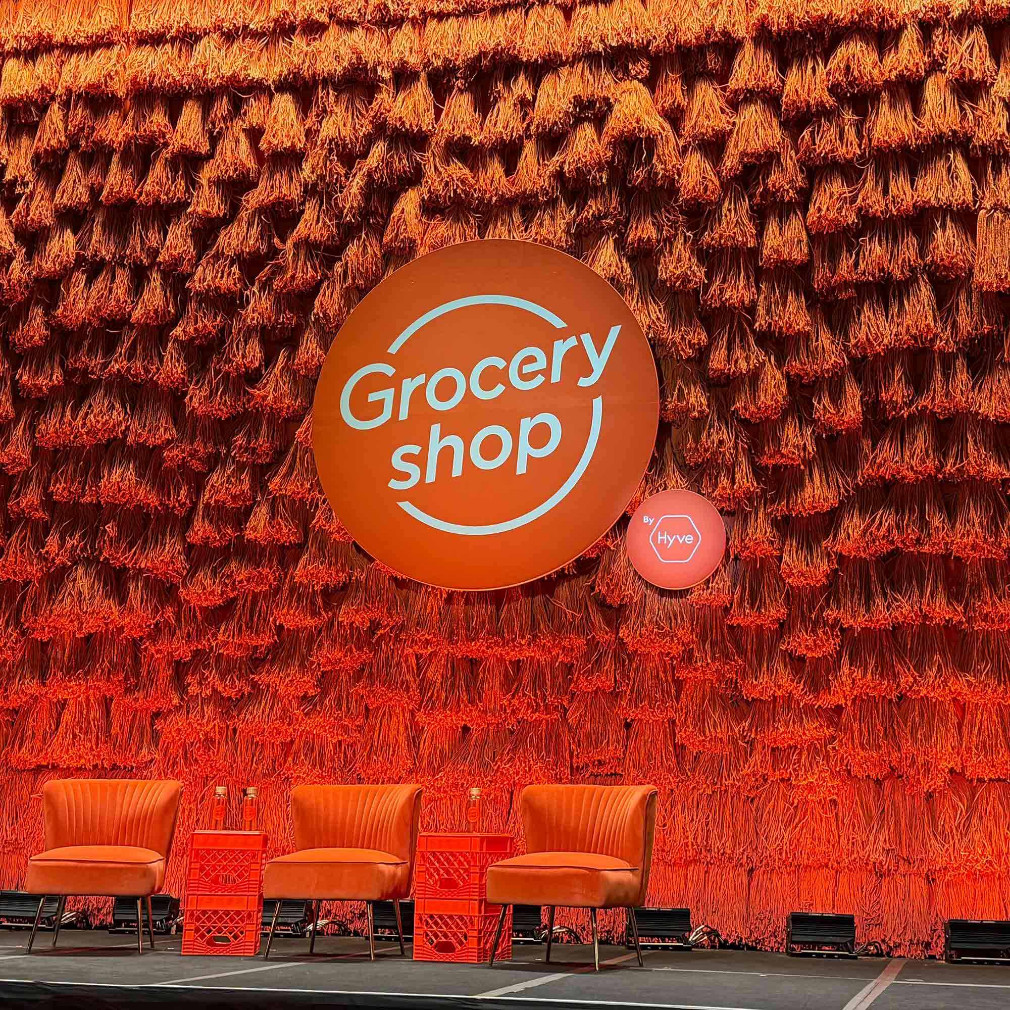 Orange mop heads hung as a backdrop behind orange grocery shop logo and orange chairs