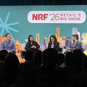 Four-person panel discussion on teal-themed NRF stage, two women and two men engaged in conversation about retail innovation, NYC skyline
