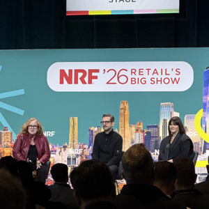 Three-person panel on teal NRF '26 stage, woman in burgundy leather jacket gesturing while speaking, man in black sweater and woman with dark hair listening, Chicago-style skyline backdrop visible.