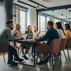 A diverse group of professionals collaborating around a table in a stylish modern conference room with large windows and natural lighting, creating an energetic and professional atmosphere perfect for corporate and business use.
