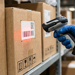 Hand in blue glove scanning barcode on cardboard box in warehous
