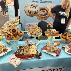 Table of cinnamon rolls and pastries on cake stands at a "Cinnamom" gourmet cinnamon rolls booth.
