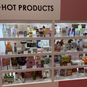 Lit display case of packaged Korean food and drink products under a HOT PRODUCTS sign at a trade show.