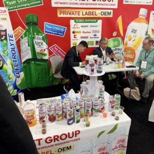 Beverage manufacturer booth with canned drink samples on a table where three men sit talking in a meeting.