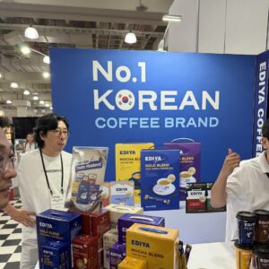 'EDIYA' coffee booth under a 'No.1 KOREAN COFFEE BRAND' banner with boxed coffee mixes and people talking.