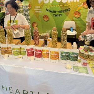 Popcorn booth with tall glass jars and a row of pouches on the table, staff behind a 'Heartland' Taiwan-inspired display.